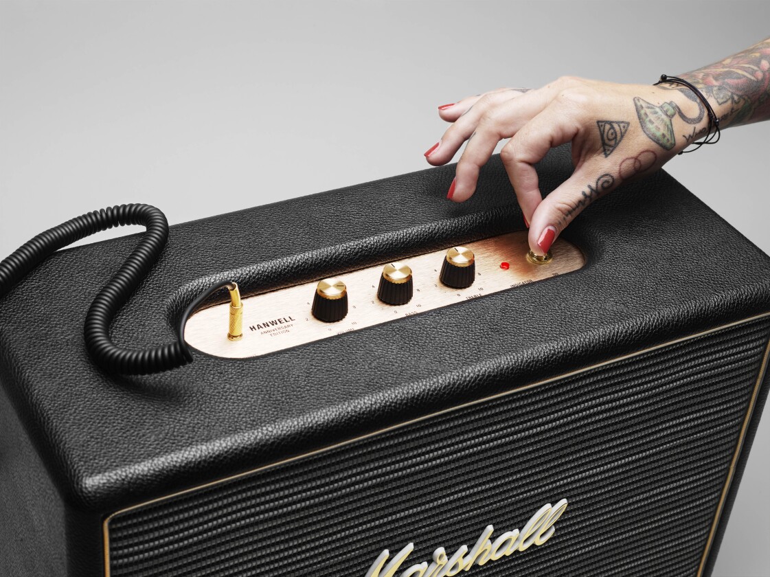 The upper face features a brushed brass metal plate that's home to classic control dials for volume, bass and treble, a source audio input jack, a retro analog power switch and a red power status light