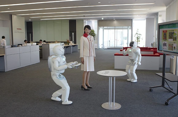 One ASIMO interrupts its presentation, to indicate that another has arrived with drinks