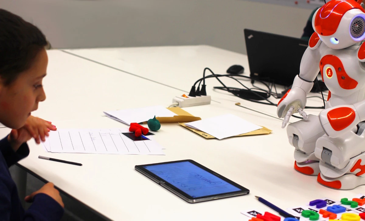 The robot writes on the tablet and then the children correct it with the stylus