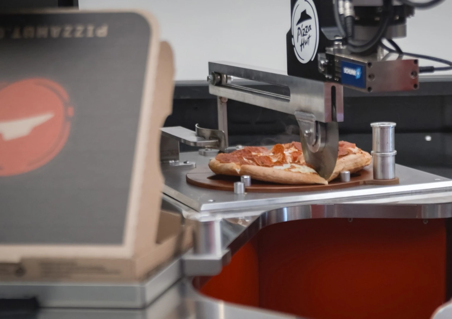 After the pizza is cooked, a robotic arm moves it to a cutting board where it's sliced perfectly into six pieces