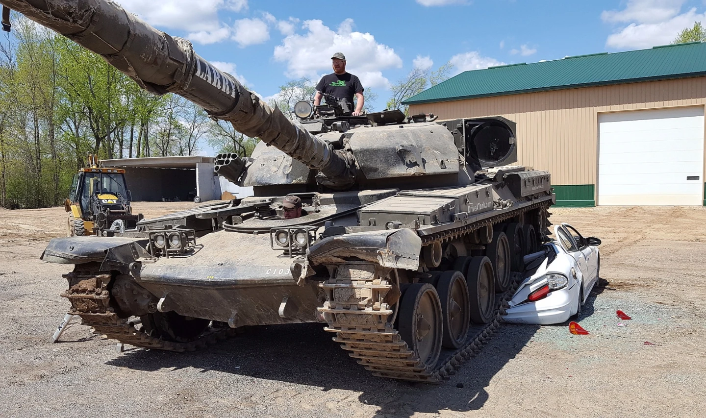 Standing atop the Chieftain FV4201 battle tank, the author surveys the machine's movement as journalist Tim Esterdahl pilots it over a hapless car