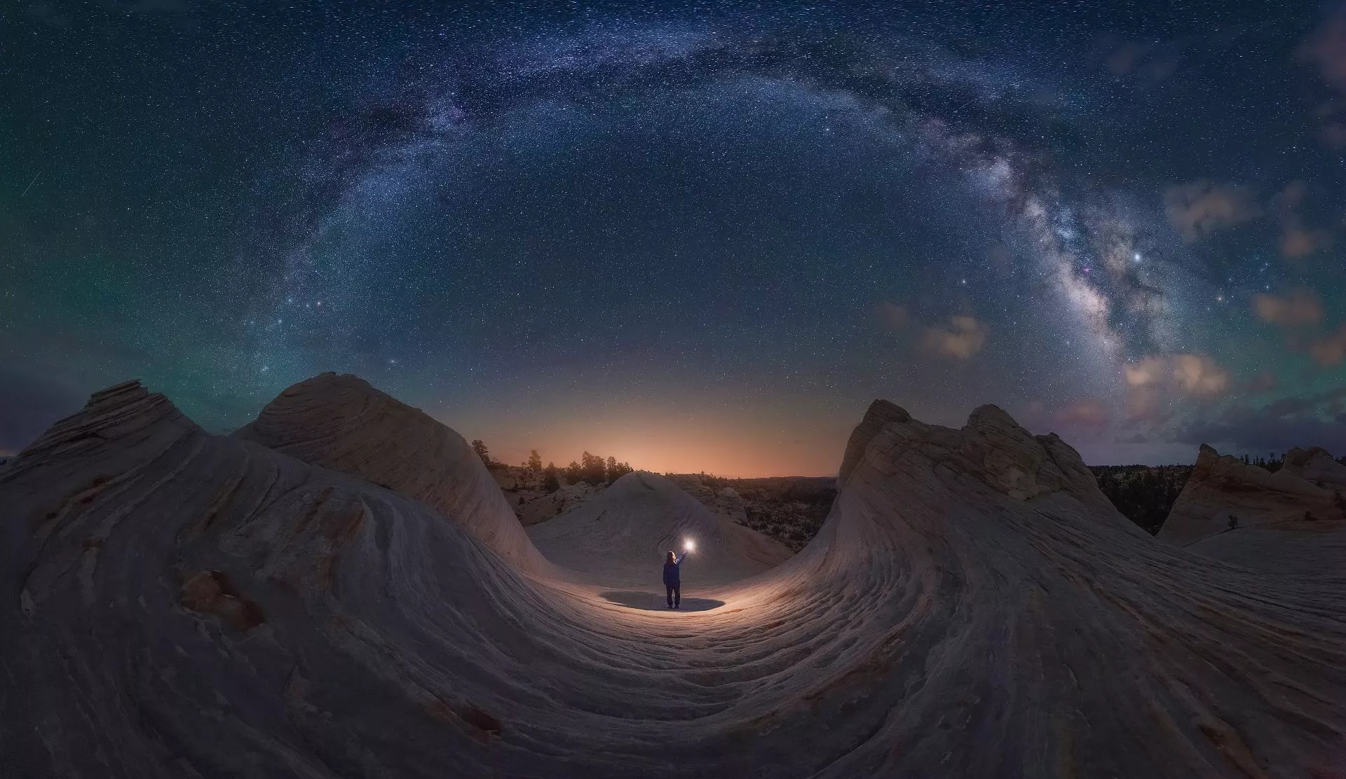 Good Night Utah, shot in Kanab, Utah, USA. Waves of rock mimic the arch of the Milky Way overhead, forming a makeshift circle. The Sun begins to peek over the horizon, the same color as the light cast by the figure in the center.