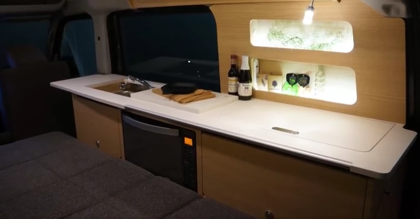 The kitchen includes an under-counter microwave, a set of shelves and an overhead cabinet