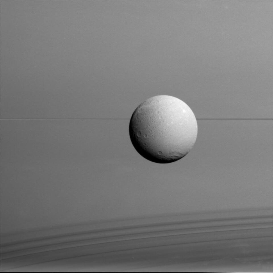 Dione imaged by Cassini at a distance of 45,000 miles (73,000 km) with Saturn in the background
