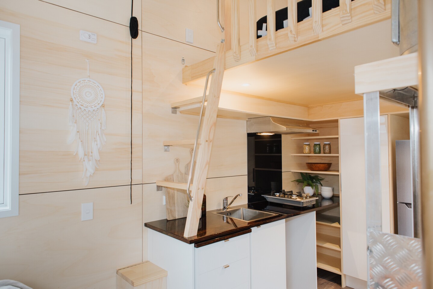 The Kahurangi Koinga Tiny House's second bedroom is accessed by a ladder that's integrated into the kitchen counter