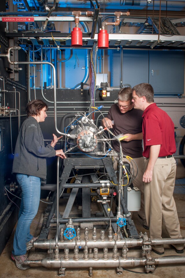 Task lead Tyler Hickman, in red shirt, and technicians inspect the rocket injector assembly