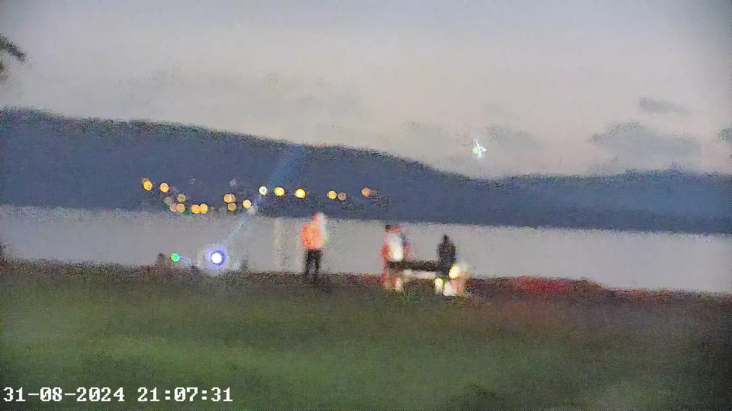 Zoom image of people in a dark seafront park with a torch beam visible