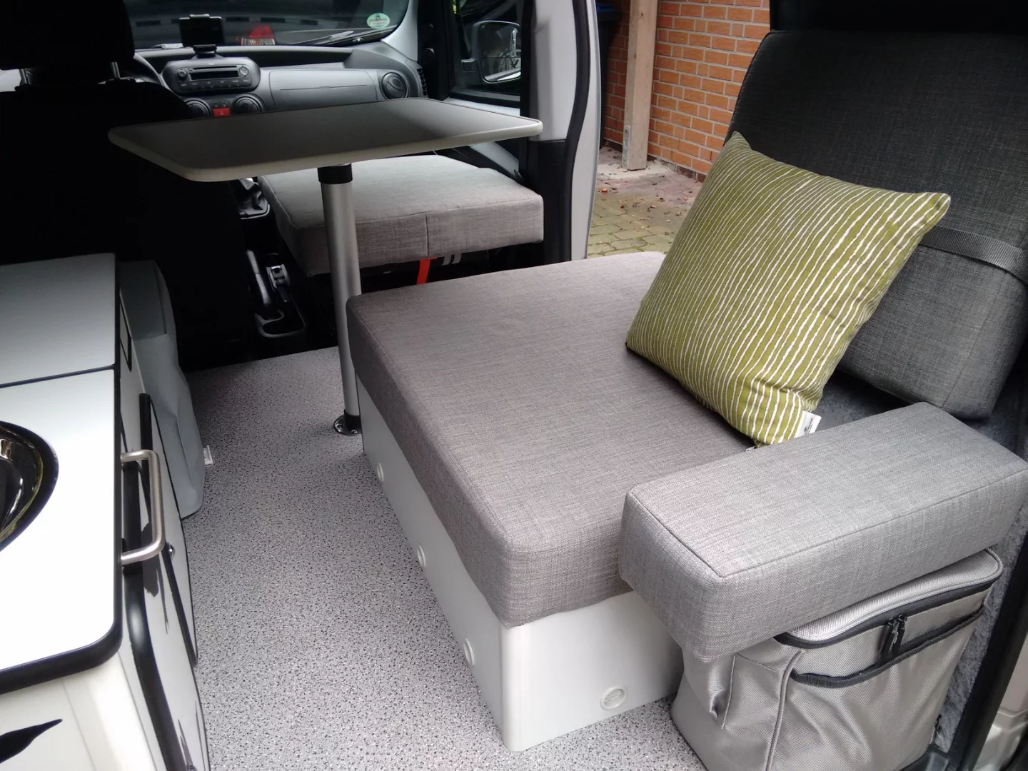 Flexcamper has created a functional, little interior for one person, complete with table, convertible seat/bed and kitchen equipment – the cushion on top of the fridge looks like a comfy armrest