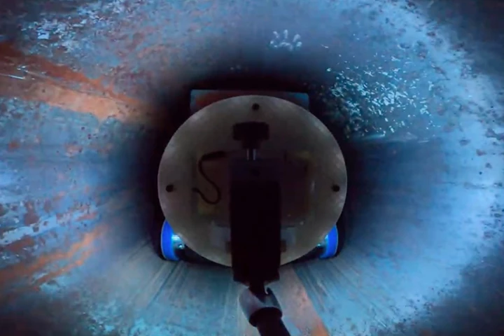 A back view of the robot, as it applies blue petroleum jelly (a stand-in for a fast-hardening resin) to the inside of a section of pipe