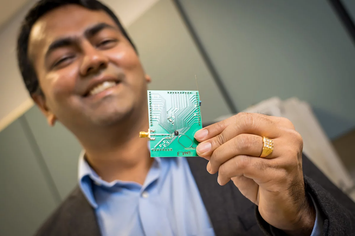 UC San Diego electrical and computer engineering professor Dinesh Bharadia holds a circuit board with the Wi-Fi chip attached