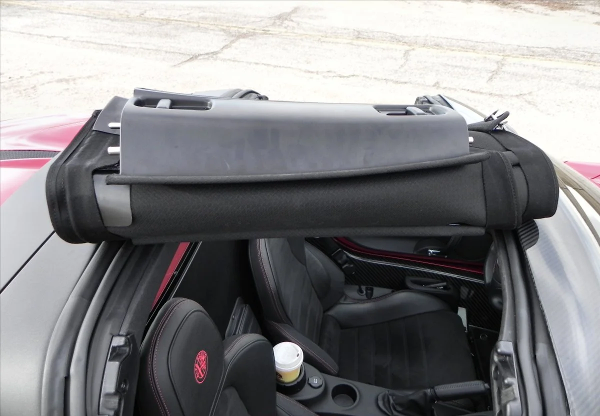 Pushing the small thumb latches above either door and unscrewing two finger-turn bolts at the front allows the top to be rolled up