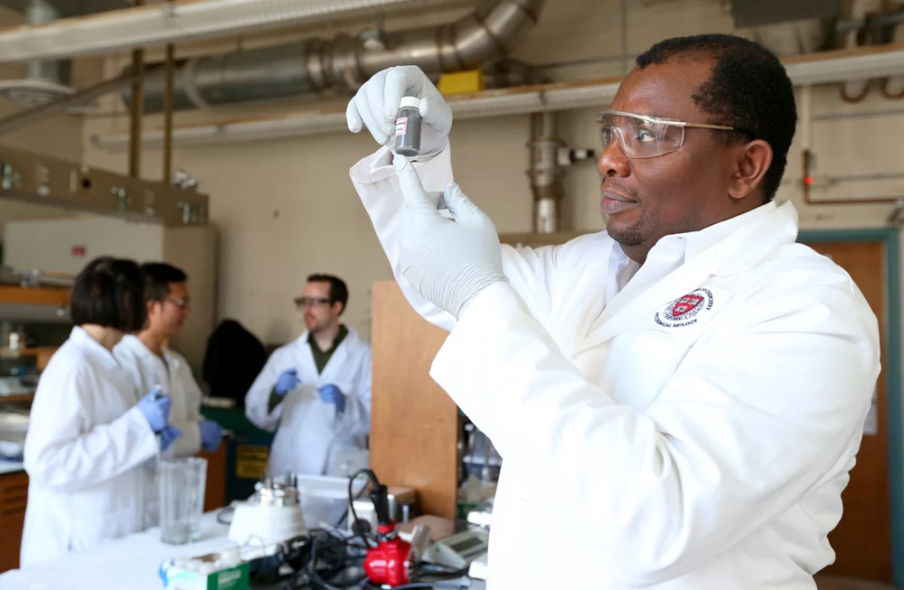 Assistant professor Martin Thuo holds up a vial of the liquid-metal particles he and his group created – behind him are, left to right, Simge Cinar, Jiahao Chen and Ian Tevis