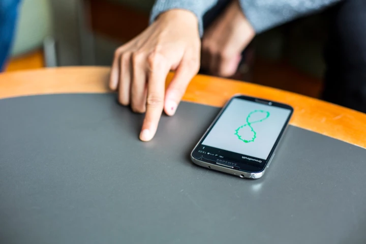 A FingerIO-equipped phone tracks a user's finger as it draws a figure 8 on the table