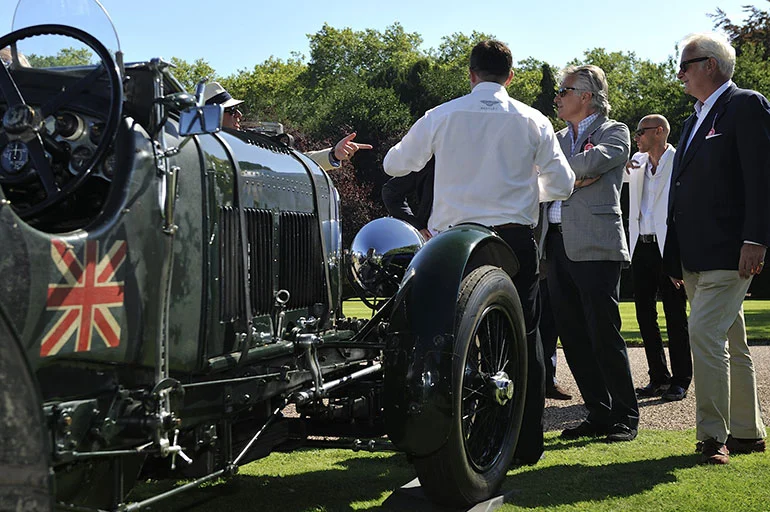 Some British chaps talking about cars next to a vintage Bentley