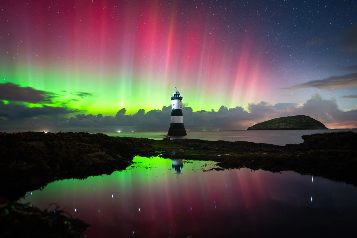Island of Aurora by Kat Lawman, taken in Wales, UK. Vibrant pillars of green and pink stretch over a lighthouse