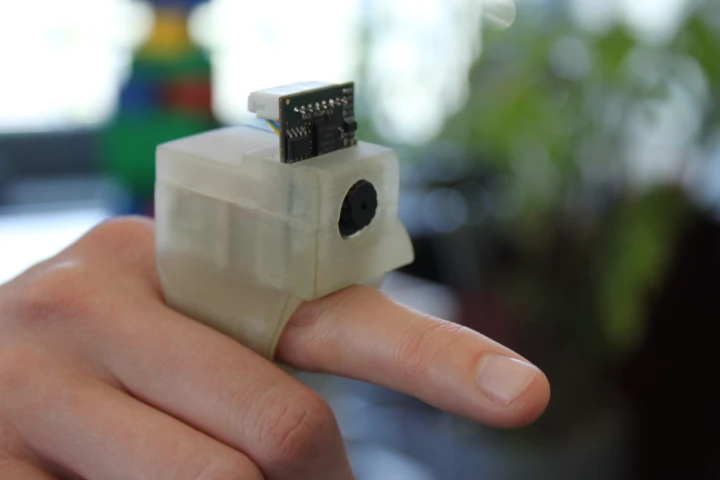 The EyeRing system features a finger-worn camera module and wirelessly connected smartphone that provide a visually-impaired user with aural feedback on objects captured by the lens