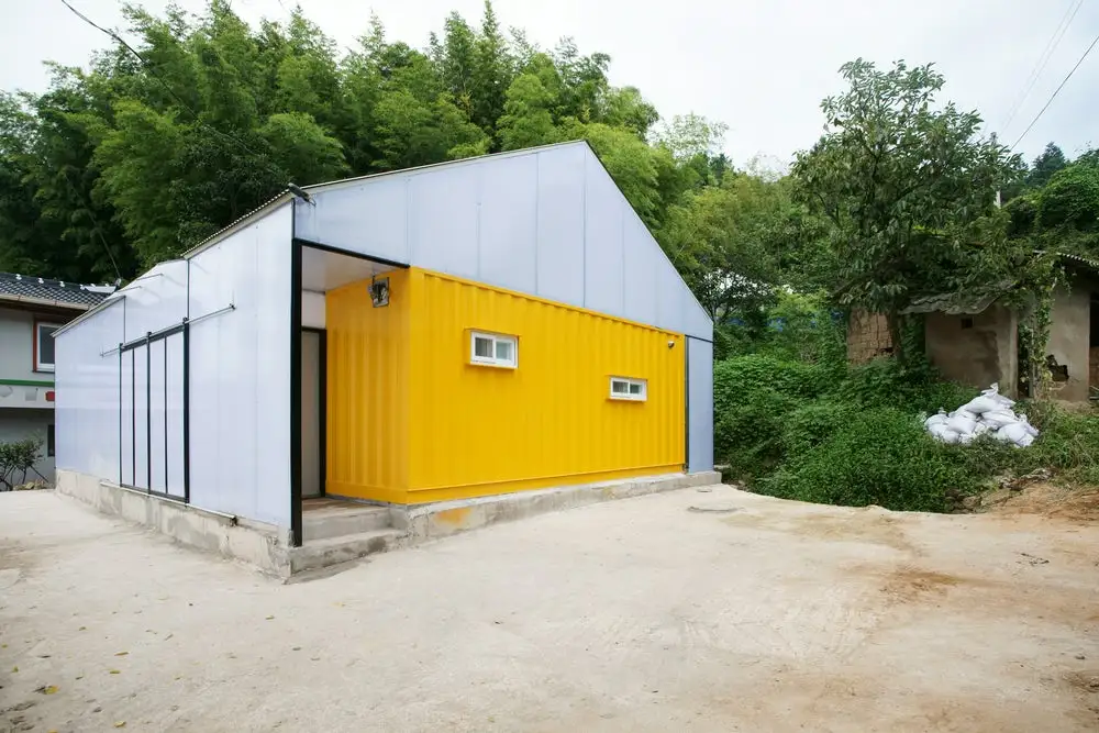 The budget-friendly Low Cost House in South Korea features three shipping containers placed within a surrounding structure in order to provide a safe and attractive home for a family of seven