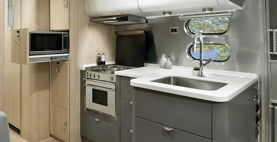 A stainless steel sink is sunk into Corian countertops alongside a three-burner stove, 6.7 cubic ft fridge and slide-out pantry