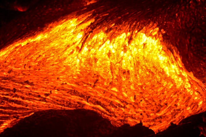 Molten lava flowing into the Pacific Ocean on Big Island of Hawaii, as ocean waves splash onto the rocks and flowing lava
