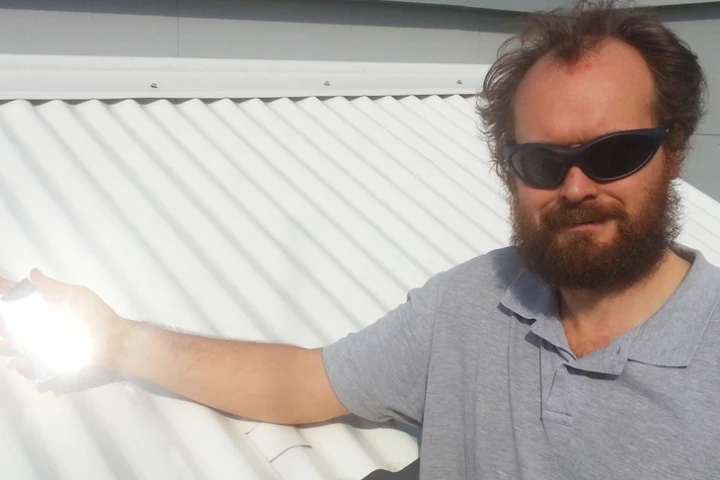 Dr Angus Gentle holding a piece of the special material over an existing cool roof used in testing