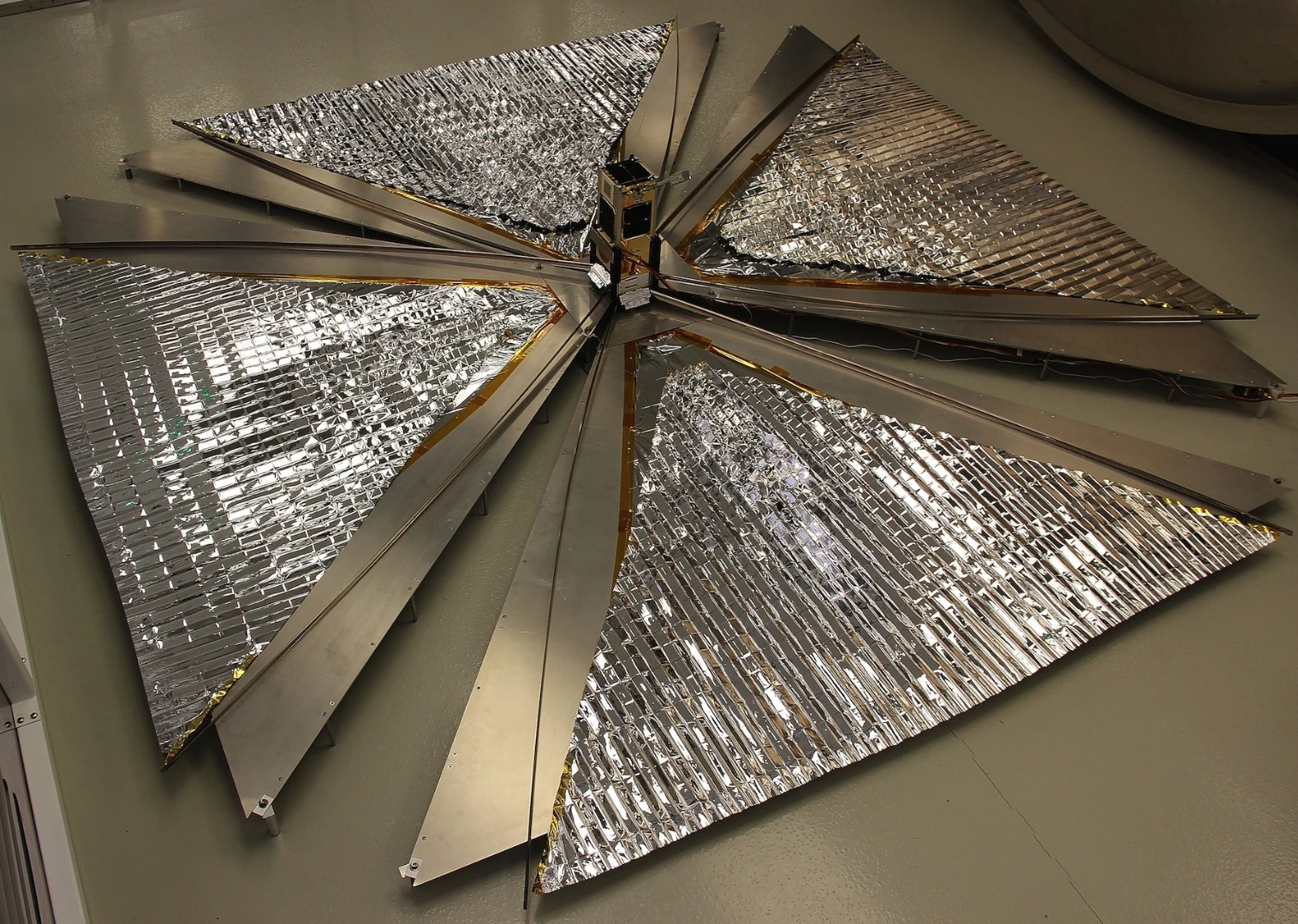 The CanX-7 satellite with its 1 square-meter (10.78 sq ft) drag sails unfurled, in a test before launch