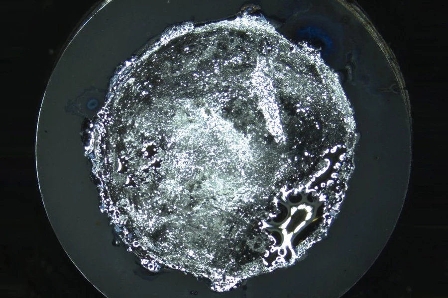 A metal electrode (the textured inner circle) sits on a grey disc of solid electrolyte, with dendrites starting to form on its surface