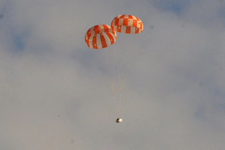 A mock Orion spacecraft descends under two main stage parachutes