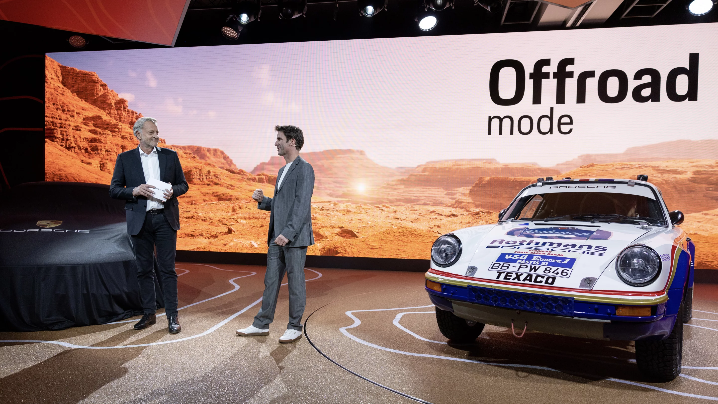 Porsche Executive Board member Detlev von Platen (left) and pro driver Romain Dumas get ready to pull the cloth off the 911 Dakar at the 2022 LA Auto Show