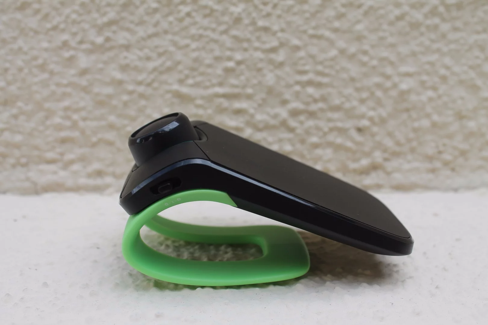 A lime green MINIKIT Neo 2 HD in profile, showing its clip for fitting around a car's sunshade to be easily placed to make and receive phone calls