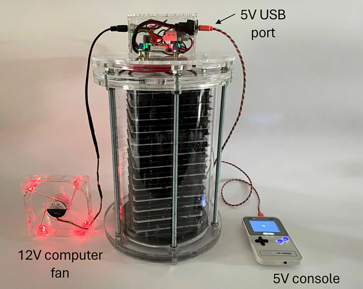 An ec3 supercapacitor prototype, made by stacking ec3 electrodes sandwiched by porous separators soaked in electrolyte, seen powering a computer fan and a game console