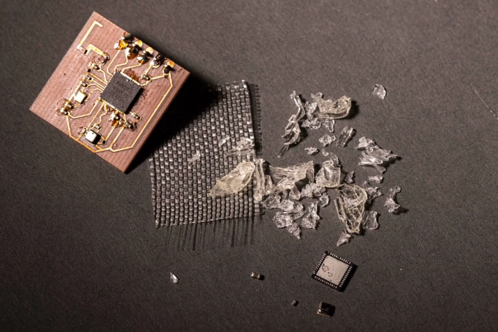 From left to right is a vitrimer-based printed circuit board, a sheet of harvested glass fibers, chunks of gelatinous vitrimer polymer that have been removed from a board, and harvested electrical components