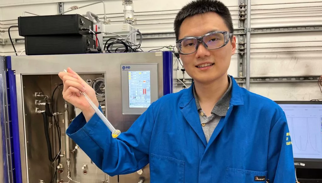 Study author Zihui Zhou with a test sample of COF-999, standing in front of an analyzer that measures CO2 adsorption