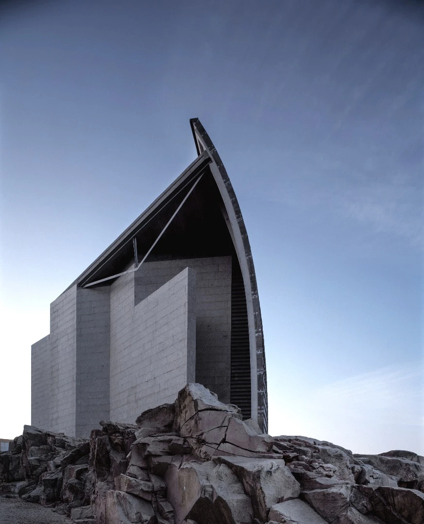Domus Museum's seaside-facing exterior forms a curved protective wall, resembling a windsail or a shell, that is clad in slate panels