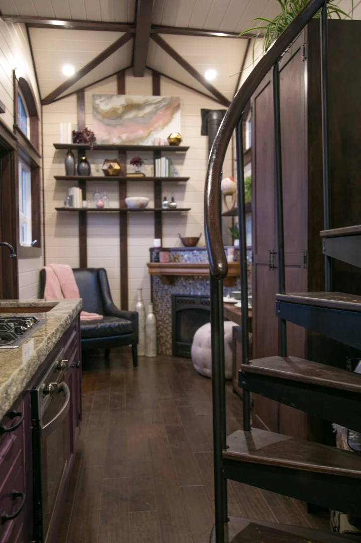 The Tudor-style tiny house's living room includes a seating area, gas fireplace, and lots of shelving