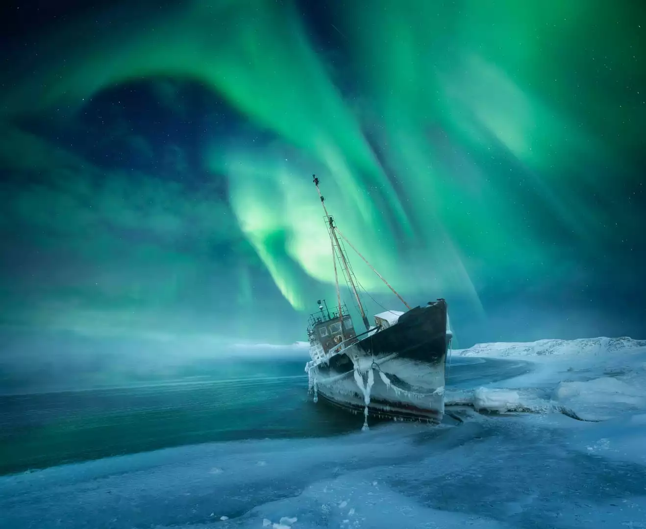 For the Northern Lights by Aleksey R., taken in Teriberka, Russia. An eerie shipwreck along the coast of the Barents Sea juts into a sky awash with green and blue aurora.