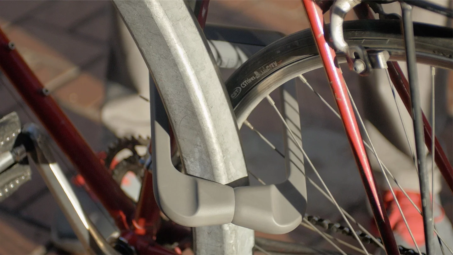 The Grasp Lock is made from hardened steel covered in soft plastic (to minimize paint scratches), and features a hinged shackle that clamps on and off in a caliper-like fashion