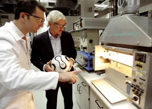 Thomas Michaelis of Bayer MaterialScience, and football player Rudi Völler with a test plant for the processing of thermoactivated adhesives. Such a system based on a waterborne polyurethane dispersion from the Dispercoll U product line from Bayer Materia