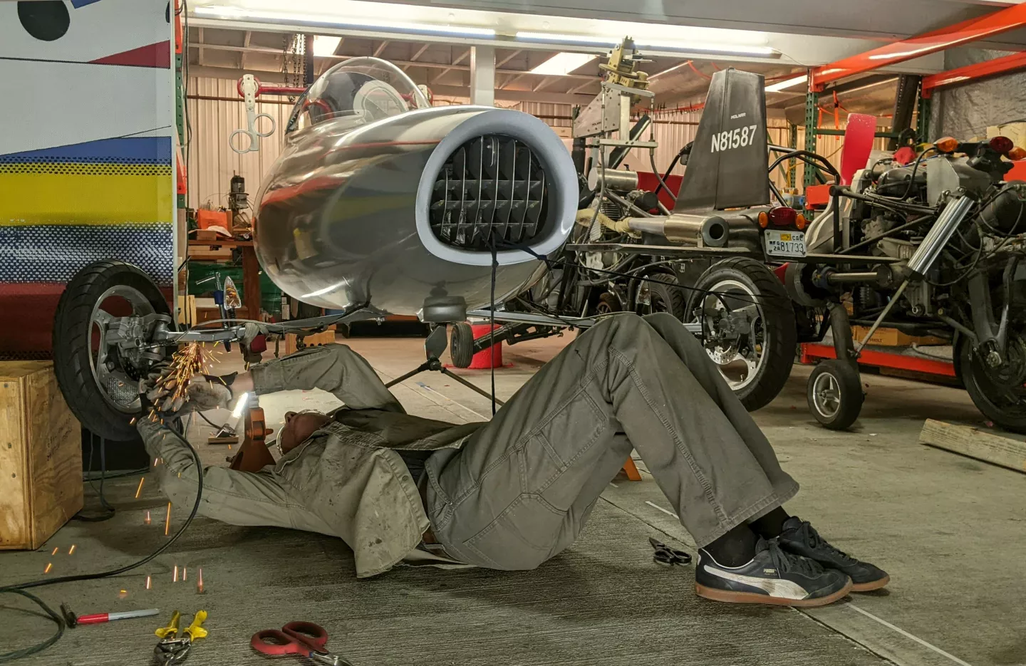 Dezső casually working on the Streetwing's front wheel in his hangar while N81587, Dezső's Molnar GT flying gyrocycle, is just hanging out and photobombing
