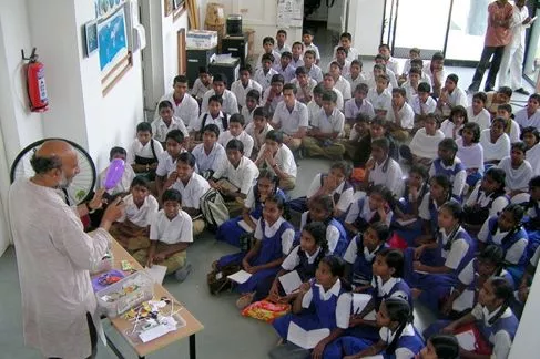 Inventor Arvind Gupta, showing a group of Indian children how to make one of his scientific toys