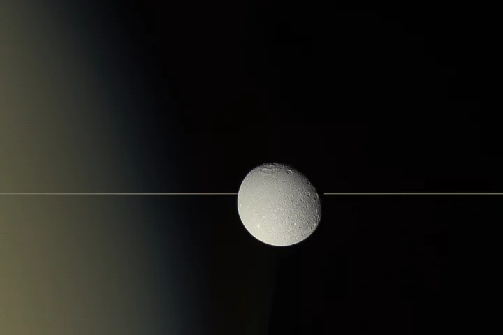 Saturn's moon Dione drifts in front of the planet's iconic rings