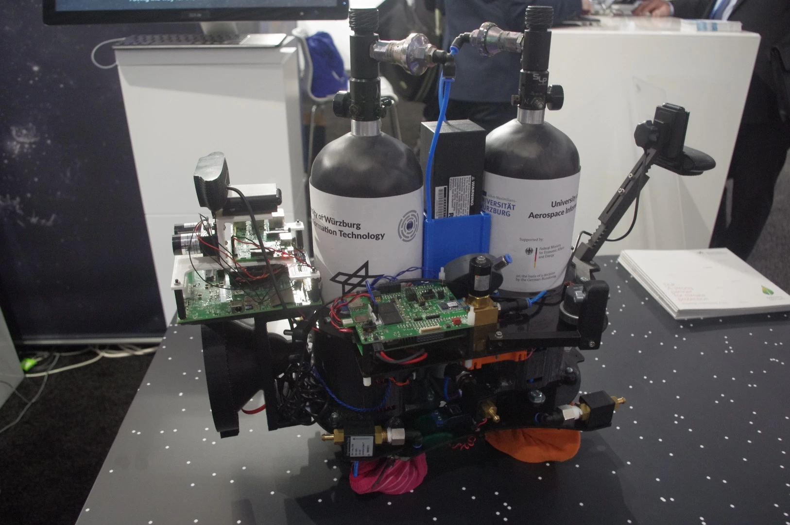 This exhibit, at the German Aerospace Center booth, is a satellite simulator. The compressed-air tanks in the center of the device allow it to float on a cushion of air so that researchers can examine different configurations and their effects on the system.