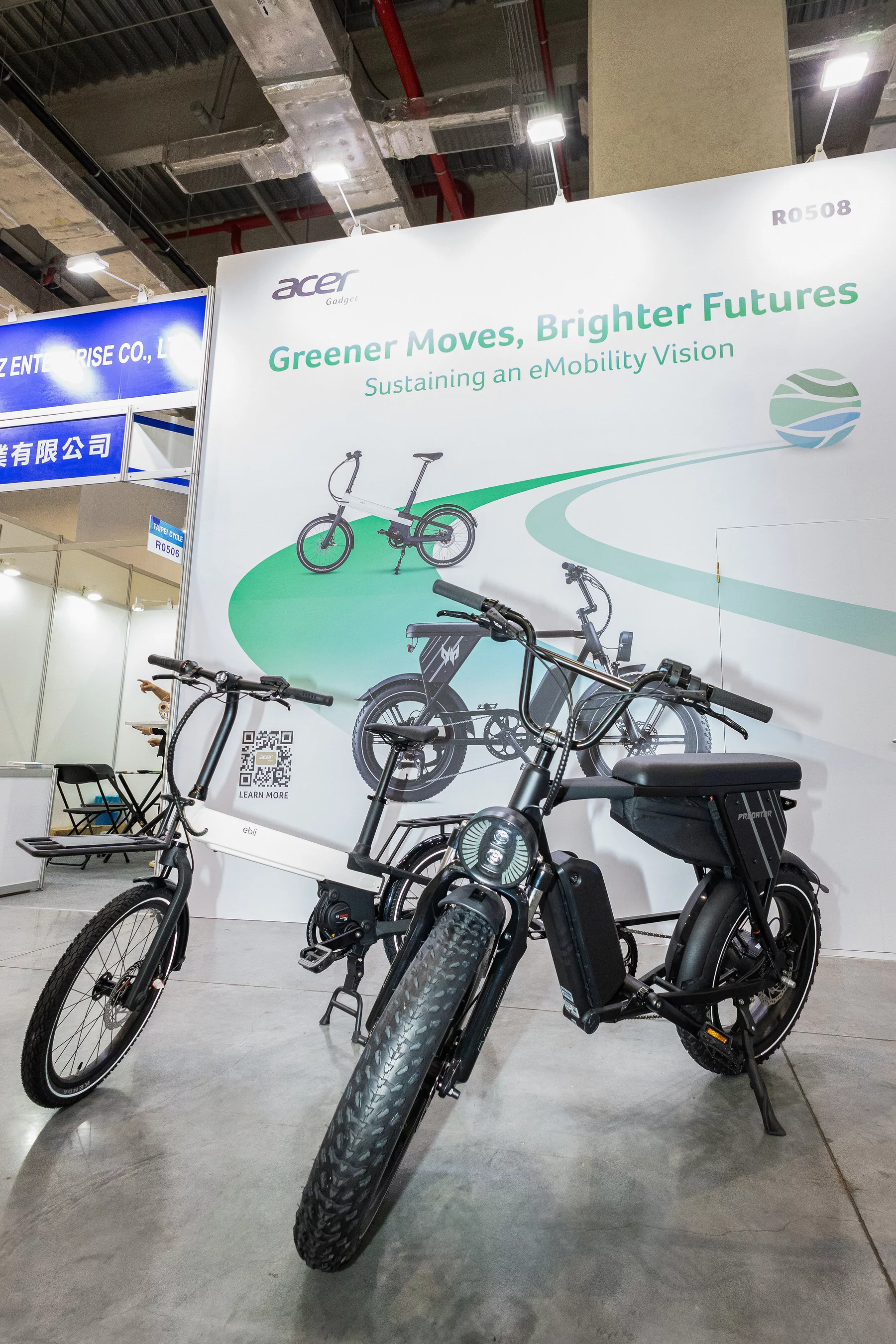 The ebii-M commuter with mounted racks front and back snuggles up to Acer's Predator eNomad-R fatbike at Taipei Cycle 2025