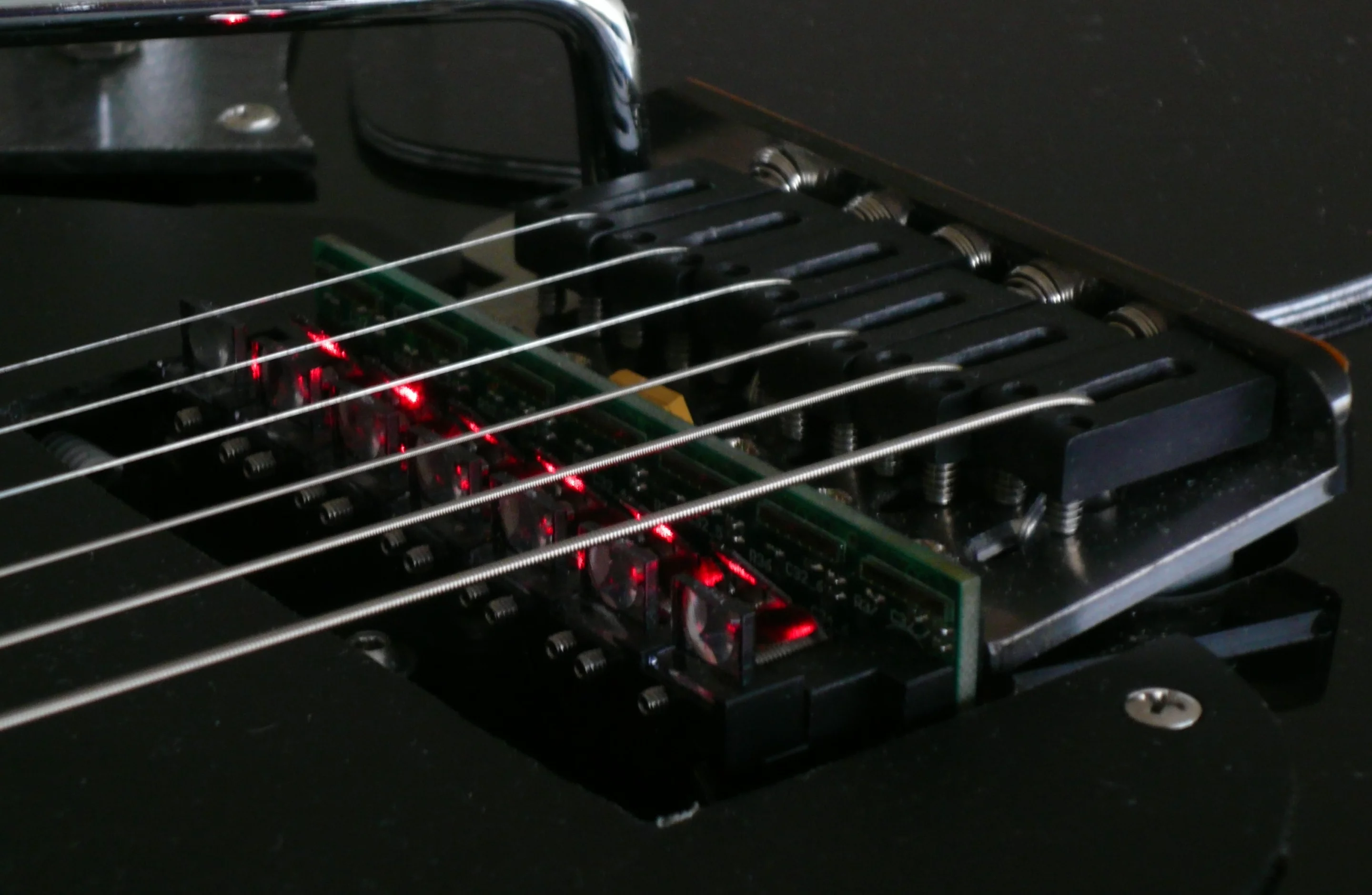 At the bridge end of the guitar, each string of the guitar has a laser diode sat underneath it that sends out a beam parallel to each string towards the end of the fingerboard
