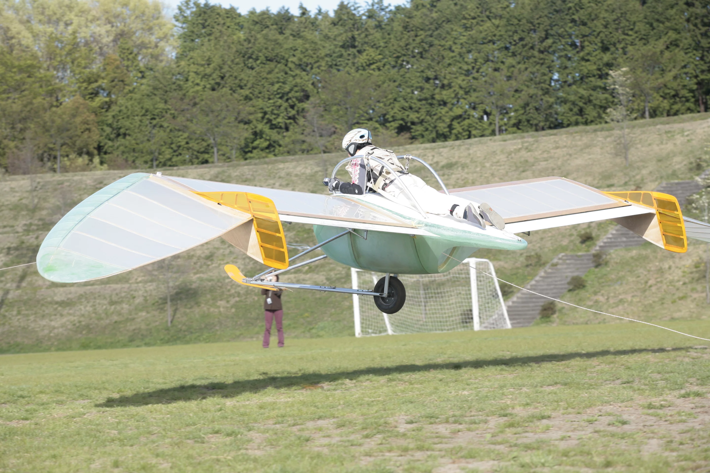 One pilot can lay down in the middle of the aircraft on a harness and adjust its pitch, roll, and direction using a set of rudder controls fitted to a pair of curved handles