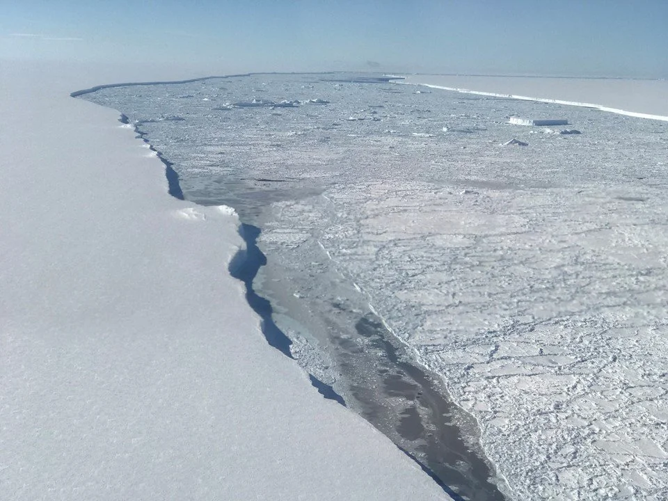 The edge of Larsen C Ice Shelf with the western edge of iceberg A68 in the distance at the top right
