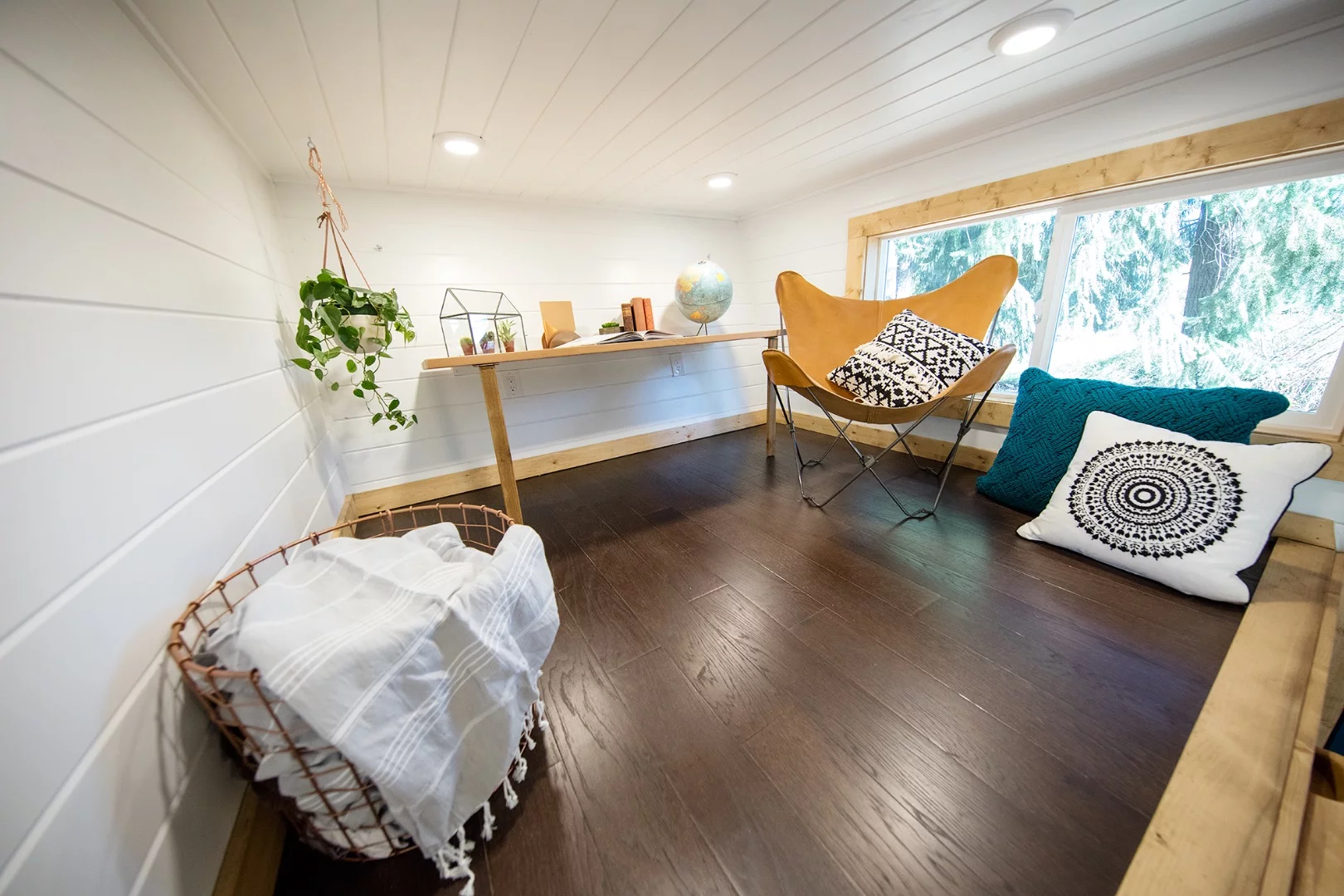 The Tiny Adventure Home has a snug lounge/office space with a small desk, chair, and cushions