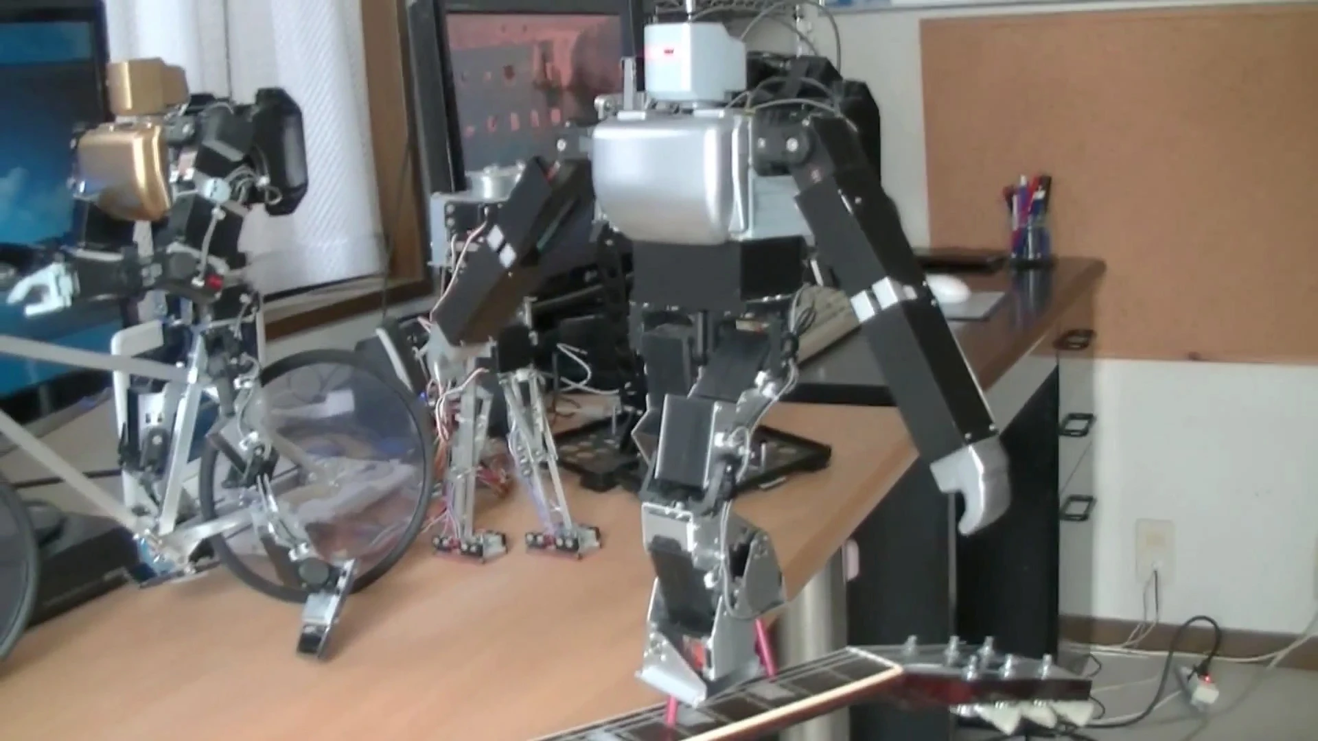 Dr. Guero's hobby robot kit balances on the neck of a guitar