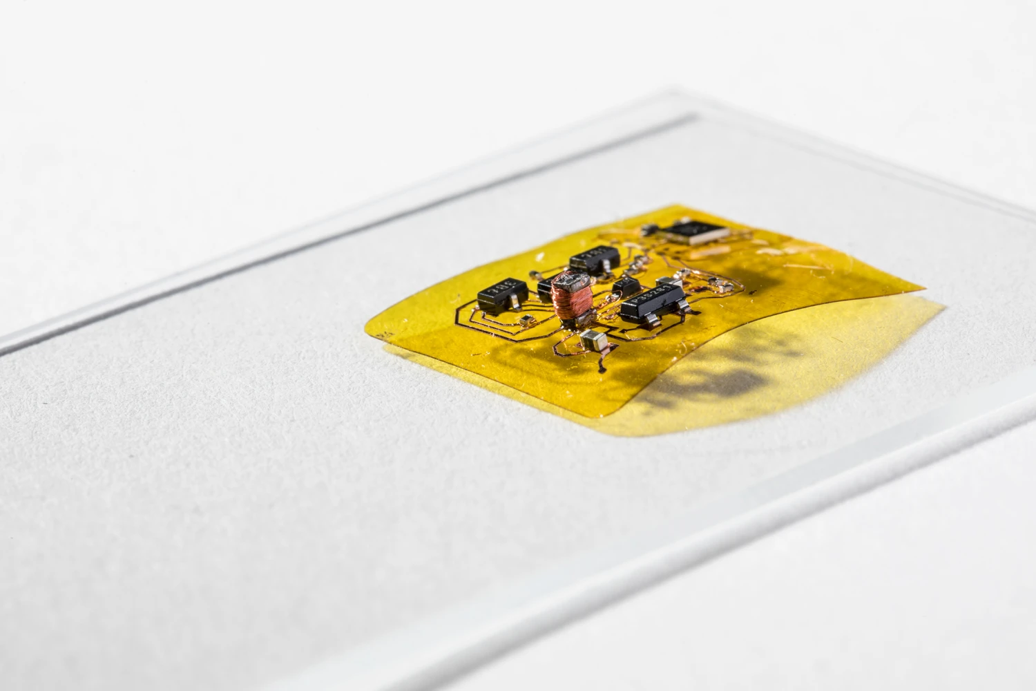 The engineers designed a flexible circuit (yellow) with a boost converter (copper coil and black boxes at left) that boosts the seven volts coming from the photovoltaic cell into the 240 volts needed for flight – this circuit also has a microcontroller brain (black square box in the top right) that lets RoboFly control its wings