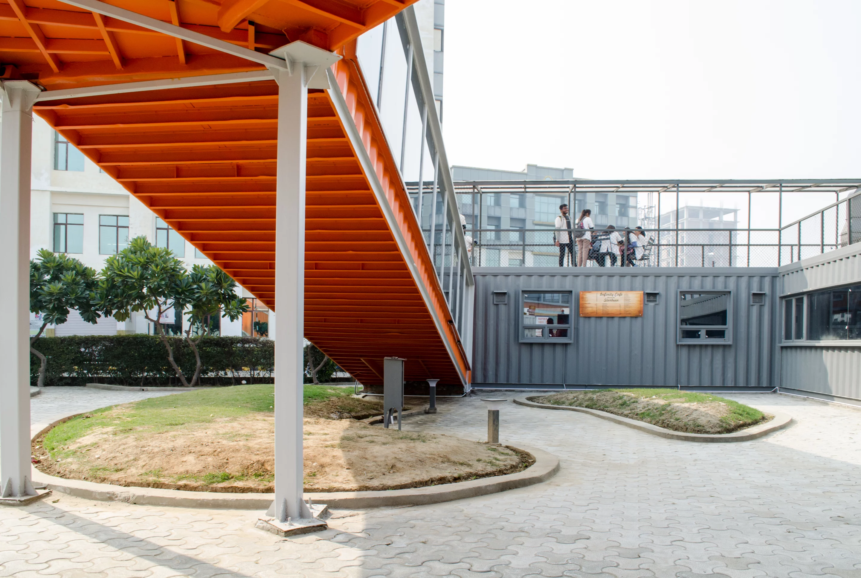 "The design idea centers around two courtyards which comprises two cafe outlets in the front ,two dynamic staircases acting as seating and providing access to the viewing decks, services (toilets) at the central container, seating areas for faculty and visitors and a lounge area for students," explains RJDL